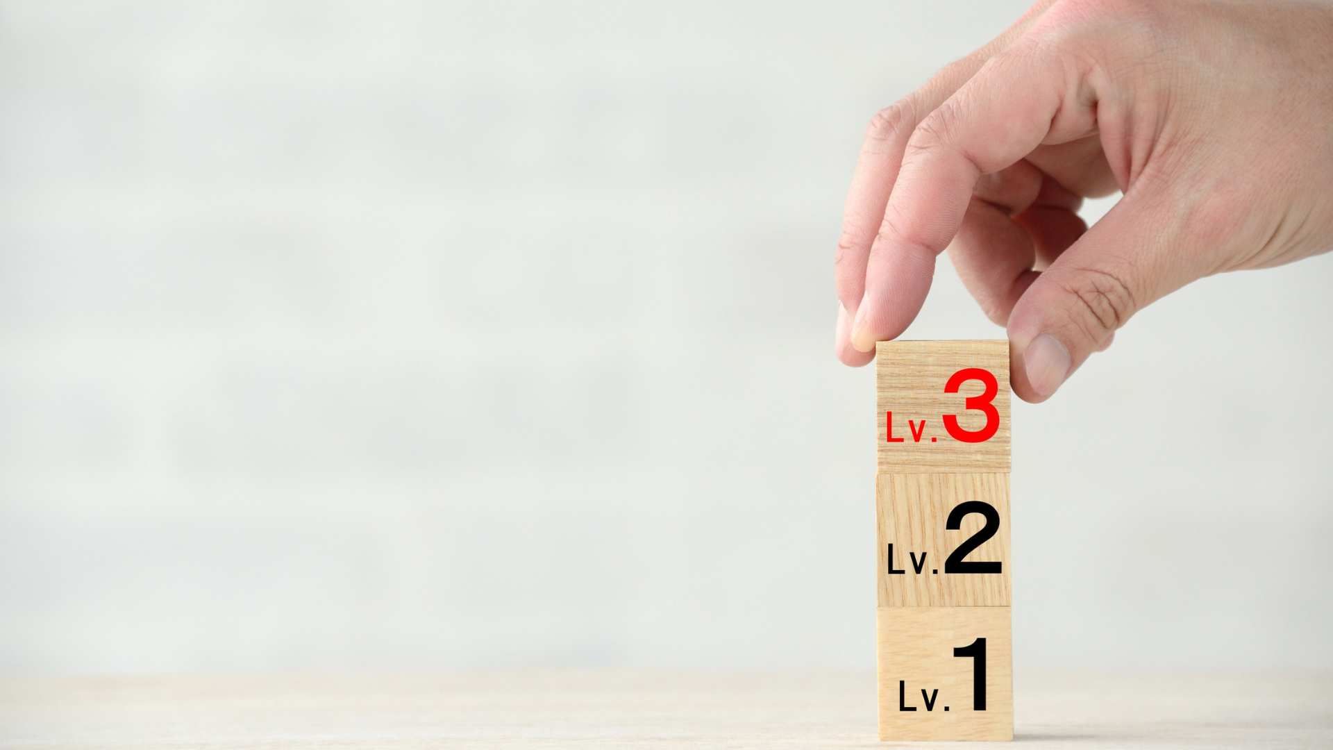 A set of wooden blocks showing levels 1, 2, and 3 being stacked by a hand, representing the range of autism levels.