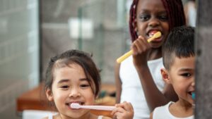 Three diverse children joyfully brushing their teeth together in a bright bathroom setting, symbolizing the development of self-care skills through ABA therapy for children with autism