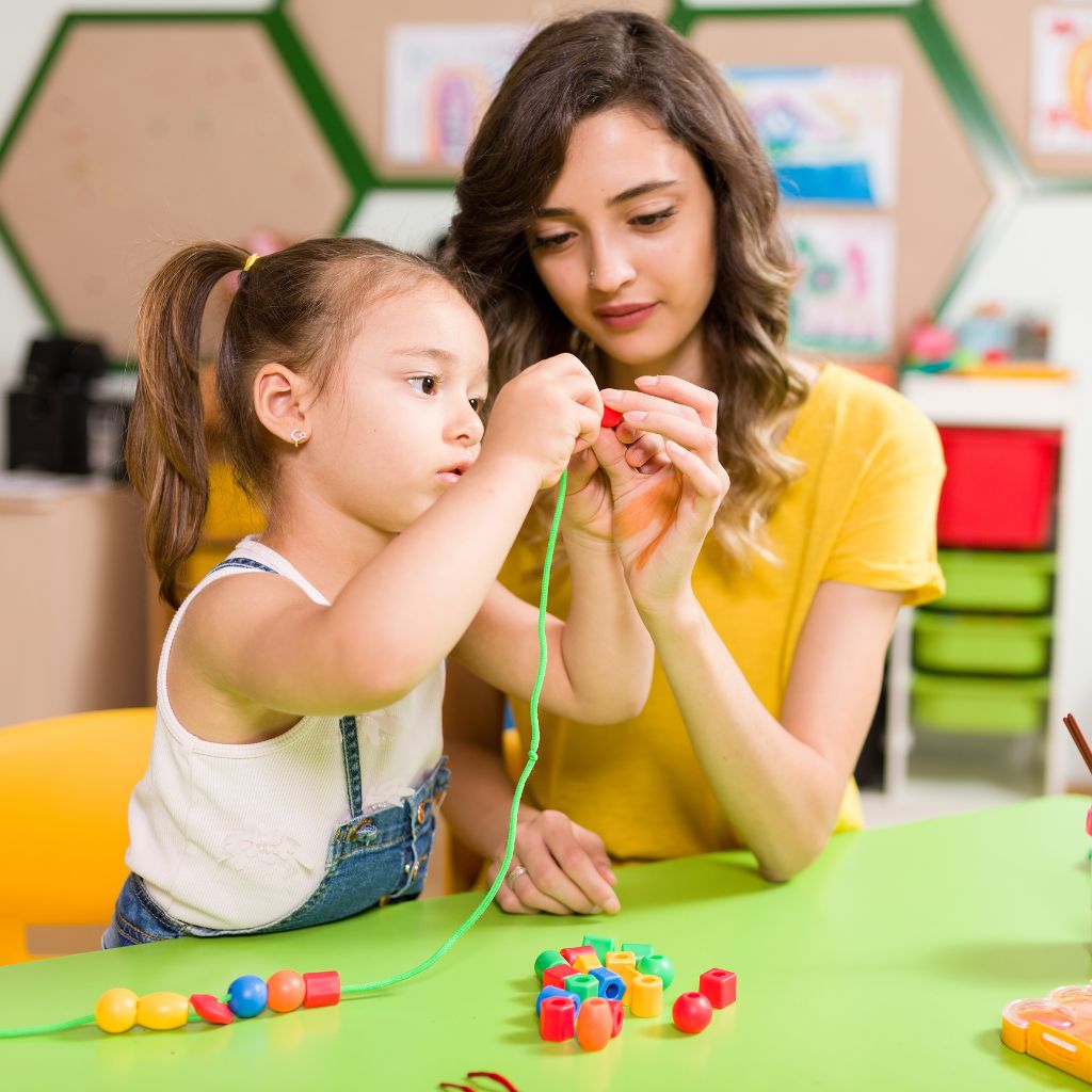 ABA therapist helping a preschool-aged child develop fine motor and communication skills during a play-based therapy session.