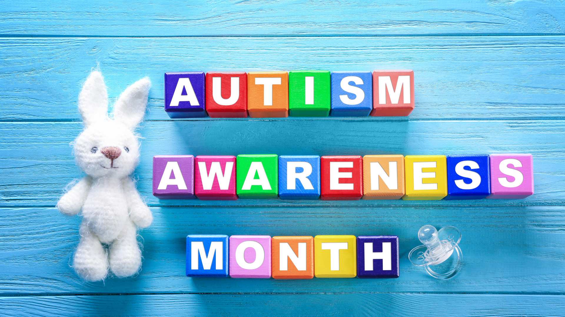 Autism Awareness Month spelled in colorful blocks with a small white bunny toy beside them