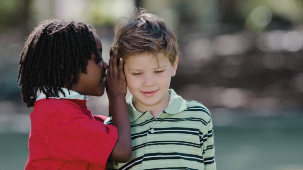 Two young children whispering together, representing the question “Does my child have autism, or is it just a speech delay?”