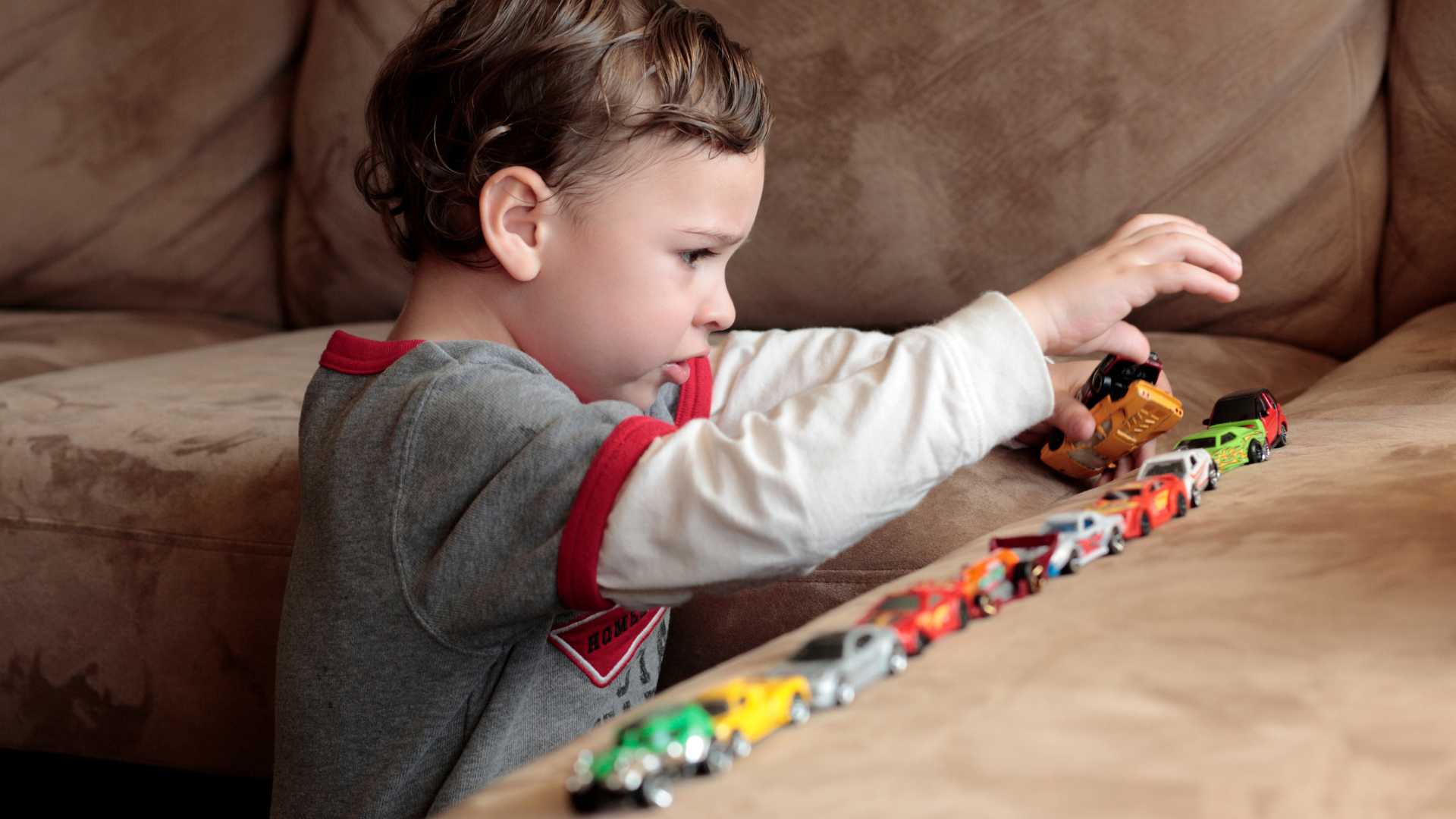 Profound autism: a toddler placing toy cars in a straight line on a couch.