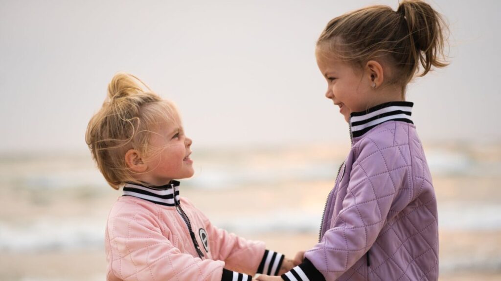 Two young children making eye contact while smiling during a positive social interaction.