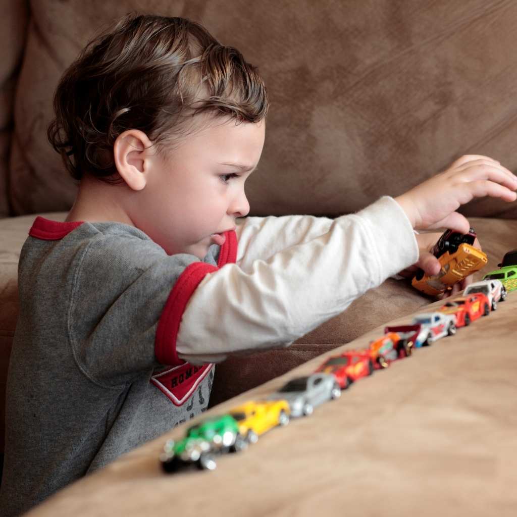 Young child focused on lining up toy cars during independent play