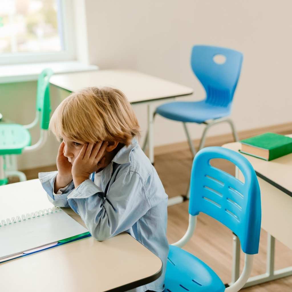 Young child sitting alone in a classroom setting during a challenging moment