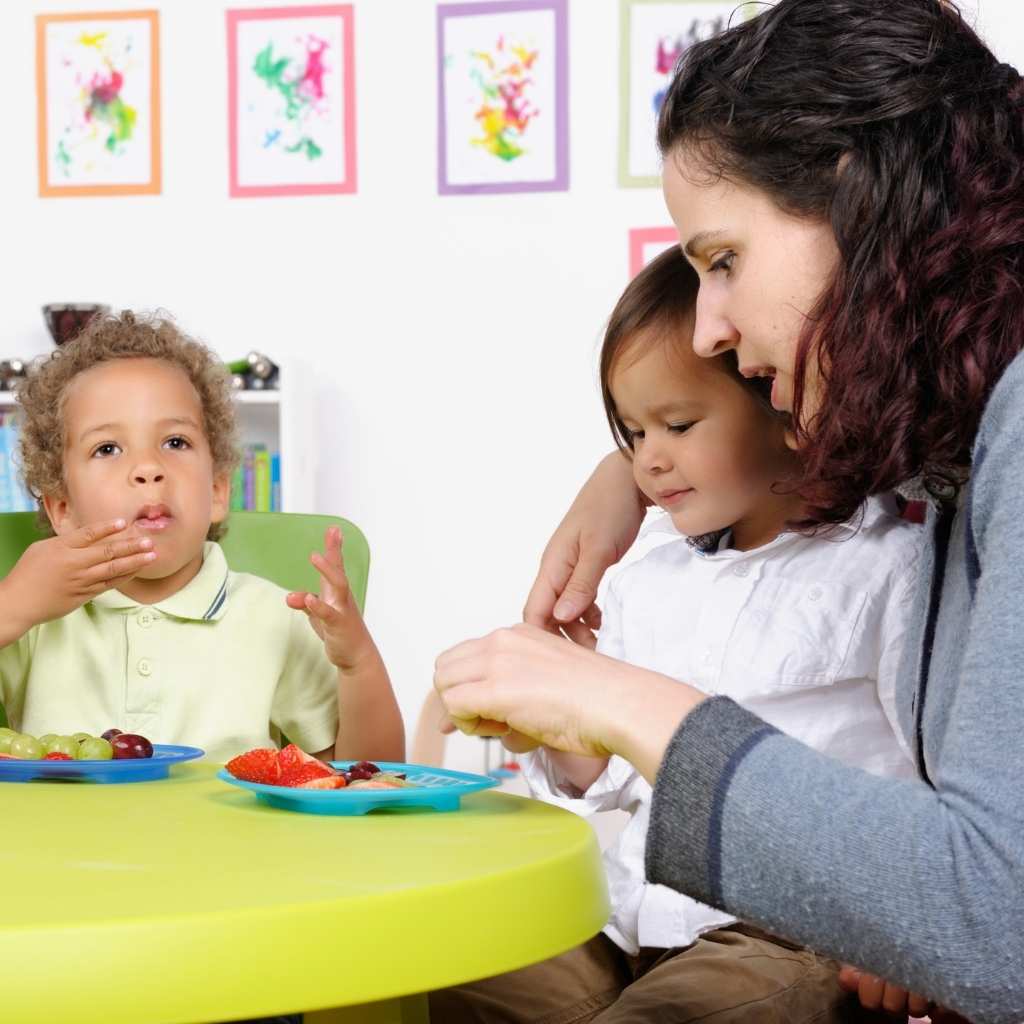 Caregiver supporting toddlers during a mealtime learning activity