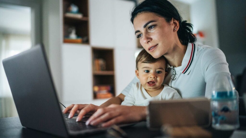 Parent holding a young child while reviewing information on a laptop