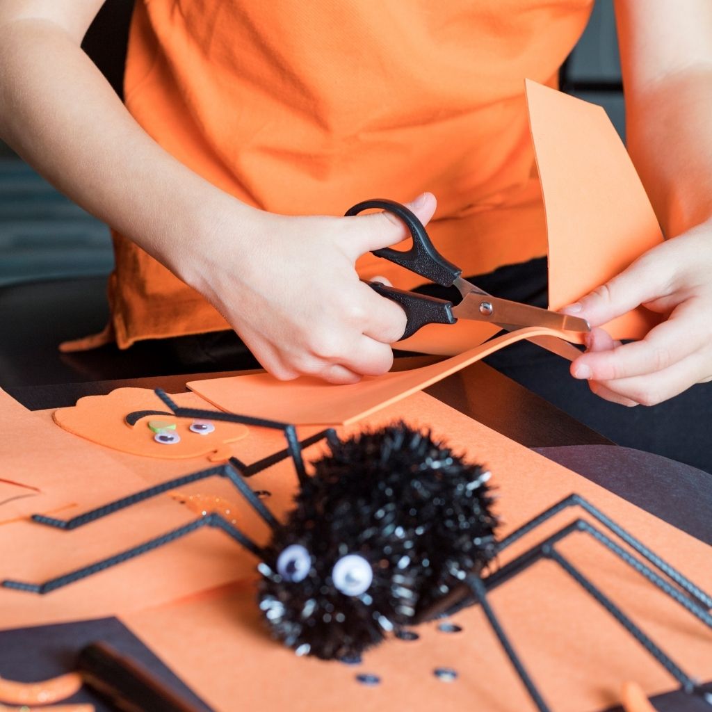 Child making a craft with orange paper and scissors as tips for autism and halloween sensory friendly activity